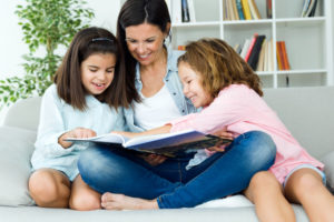 Portrait of beautiful mother with her daughters reading a book at home.